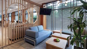 Una sala de estar moderna con un sofá azul, una mesa de centro con fruta y un televisor montado en la pared.