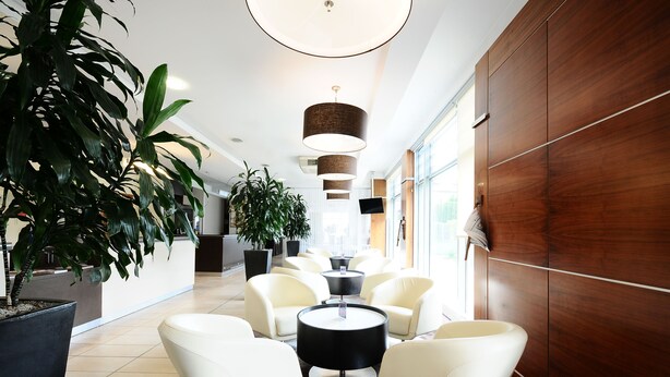 Un vestíbulo moderno con sillones de cuero blanco, una mesa negra en el centro y grandes macetas con plantas.