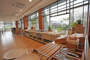 A restaurant with a long counter, wooden tables, and a view of parked cars outside.