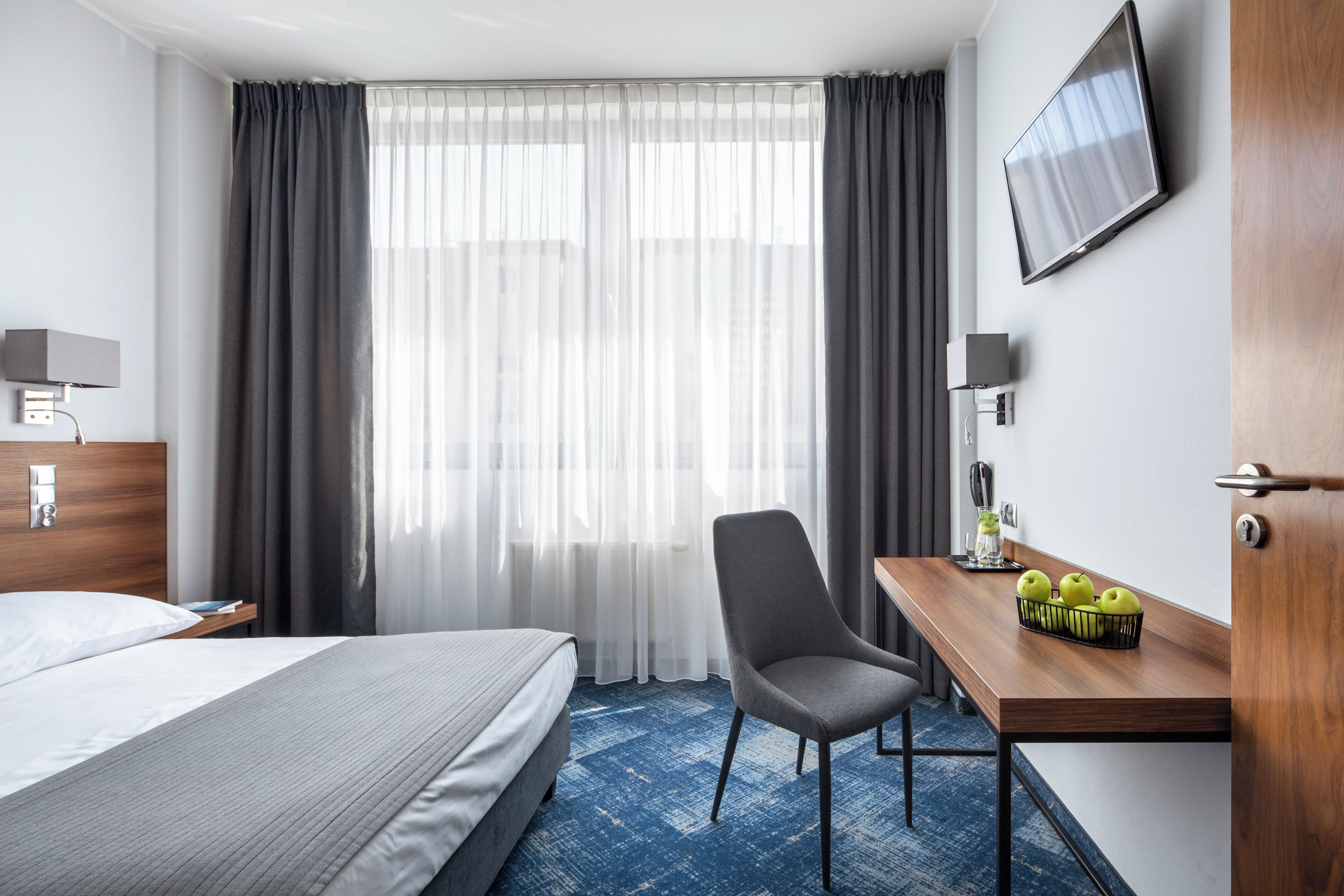 Une chambre d’hôtel comprenant un lit, un bureau avec une chaise, une télévision et un panier de fruits.