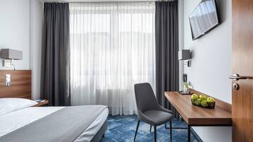 Une chambre d’hôtel comprenant un lit, un bureau avec une chaise, une télévision et un panier de fruits.