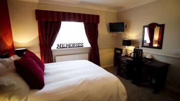 Una habitación de hotel con cama, televisor, cómoda y espejo.