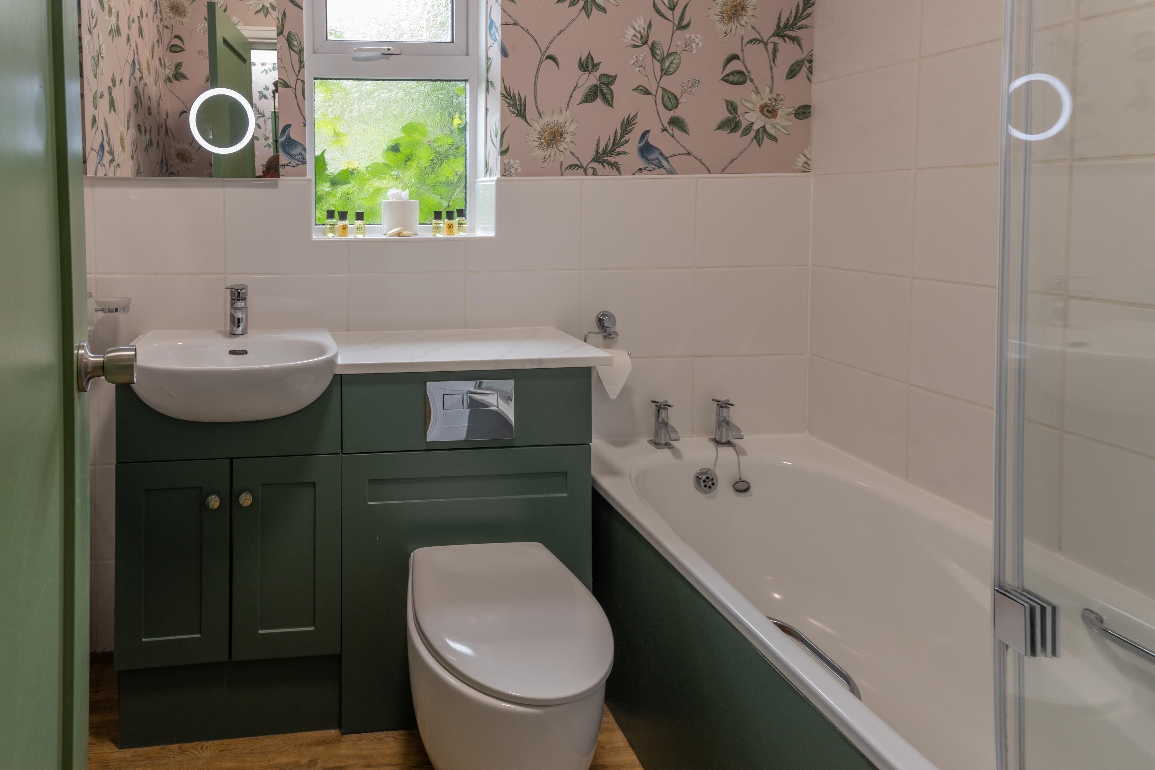 A bathroom with a white sink, green cabinets, a white toilet, and a bathtub.