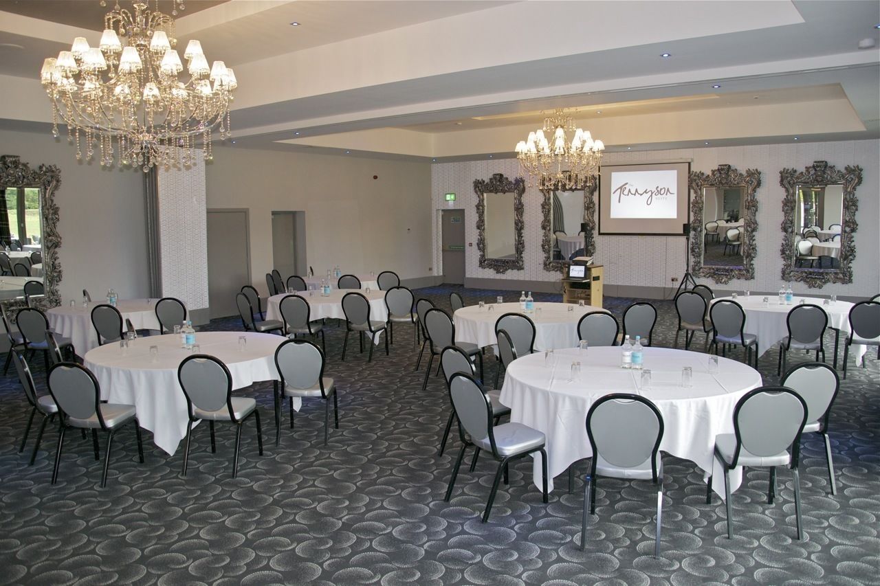 A conference room with round tables, chairs, chandeliers, and a projection screen displaying "Tennyson".