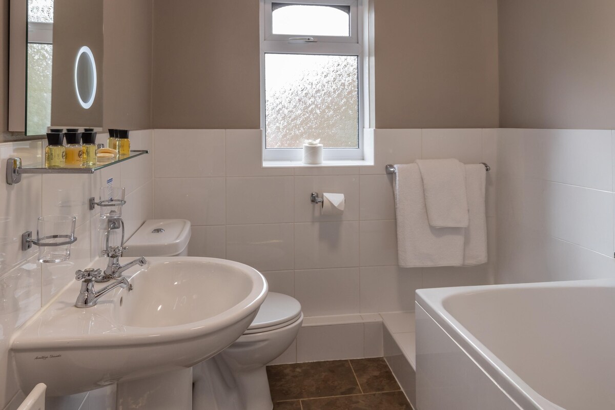 A bathroom with a sink, toilet, bathtub, and a window with frosted glass.