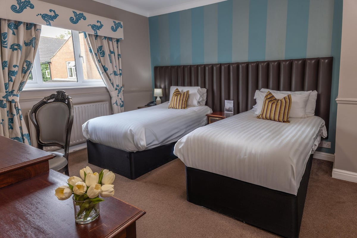 Ein Hotelzimmer mit zwei Betten, einem Holztisch, einem Stuhl und einer Vase mit Blumen.