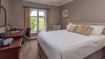 A hotel room with a large bed, a desk with a chair, a window with curtains, and a framed picture on the wall.