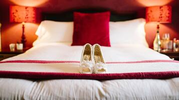 A bed with white linens and a red pillow, a pair of white shoes with floral details, and two bedside lamps with red shades.