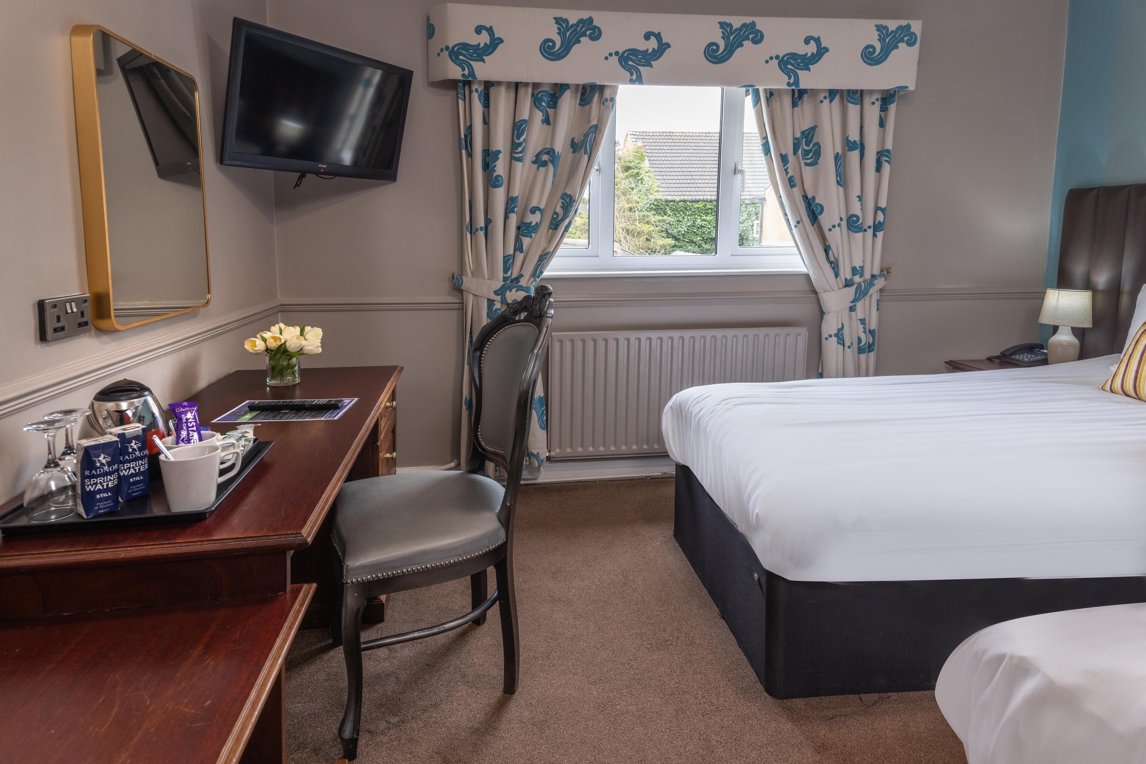 Een hotelkamer met een bed, een bureau met stoel, een aan de muur bevestigde televisie en een raam met gordijnen.