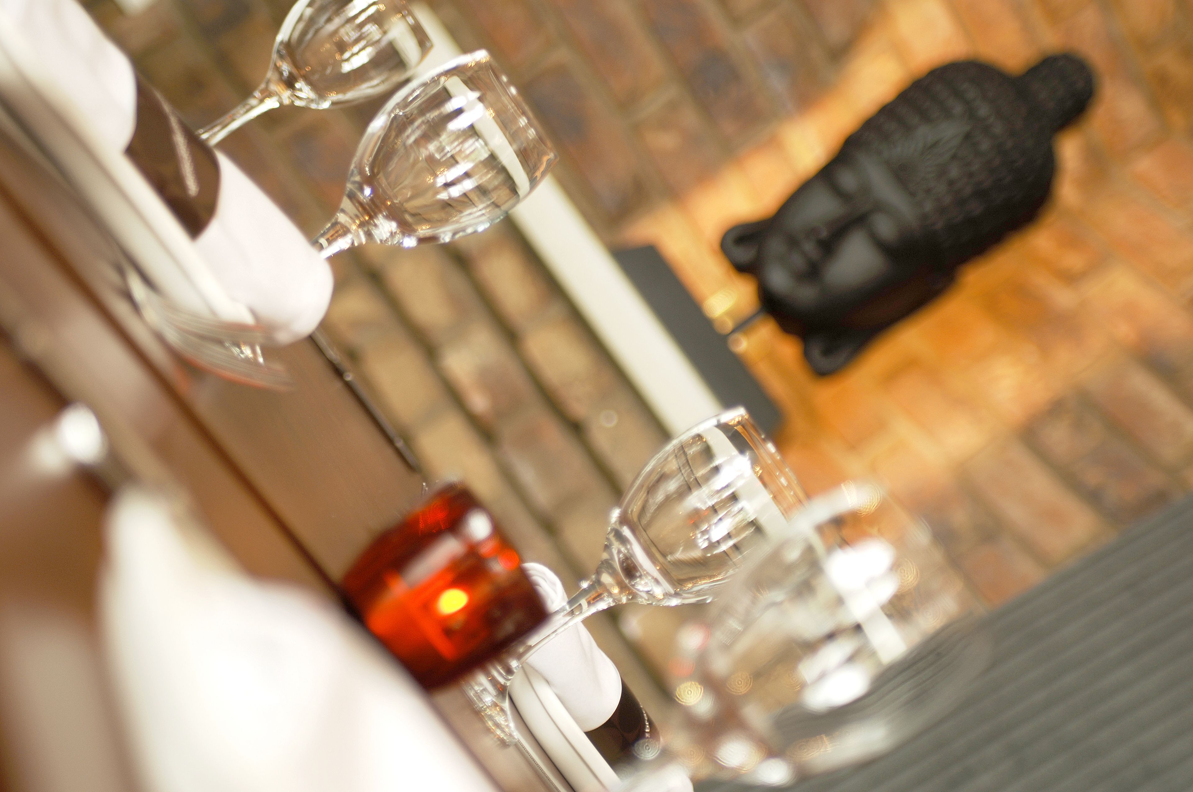 A close-up of wine glasses on a table with a candle and a Buddha statue in the background.