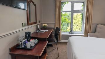 Ein Hotelzimmer mit einem Bett, einem Schreibtisch mit Kaffeemaschine, einem Sessel und einem Fenster mit Vorhängen.