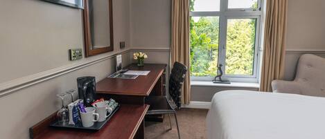 A hotel room with a bed, a desk with a coffee maker, a chair, and a window with curtains.