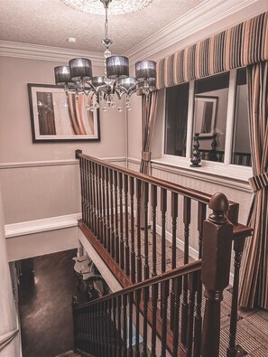 A staircase with wooden balusters and a chandelier, a framed picture on the wall, and a window with striped curtains. - Brackenborough Hotel, BW Signature Collection (Louth)