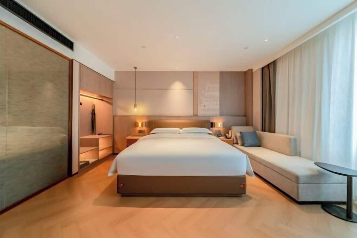 Una habitación de hotel moderna con una cama grande, un sofá, una mesita y vistas a la ciudad.