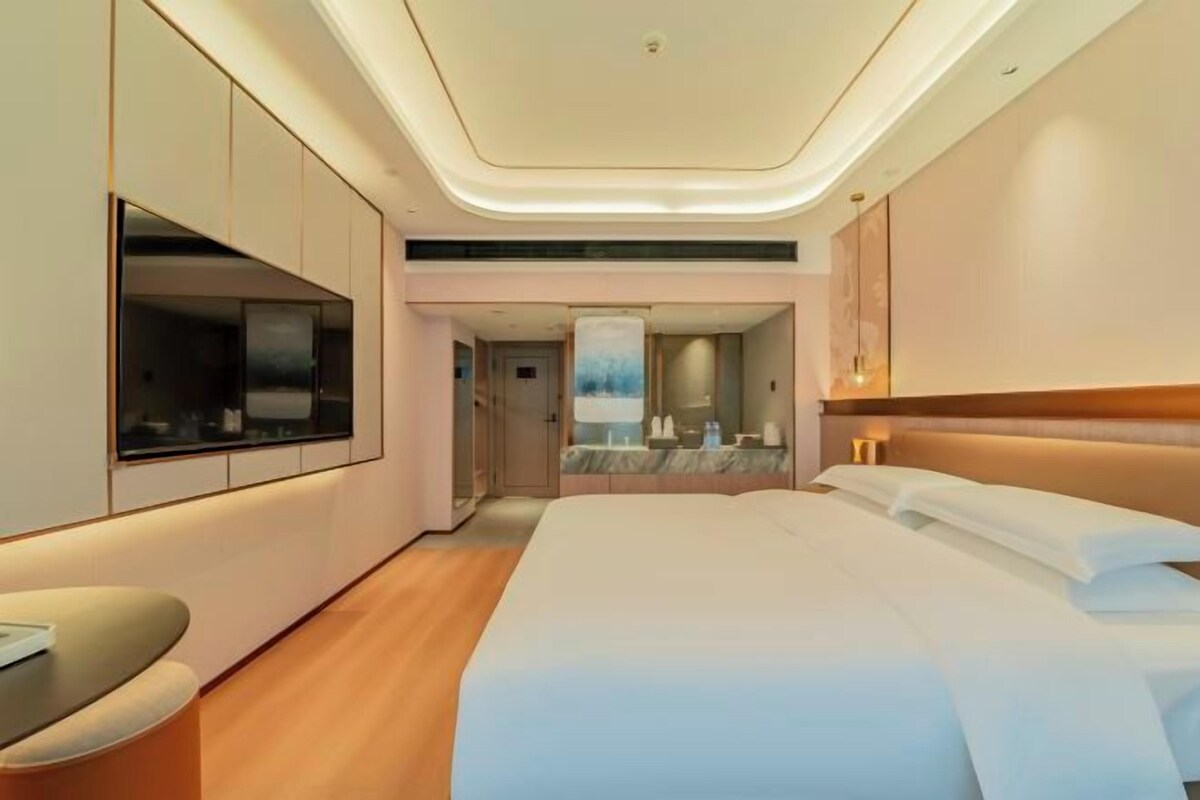 Ein modernes Hotelzimmer mit einem großen Bett, einem Flachbildfernseher, einer Sitzecke und einem durch eine geöffnete Tür einsehbaren Badezimmer.