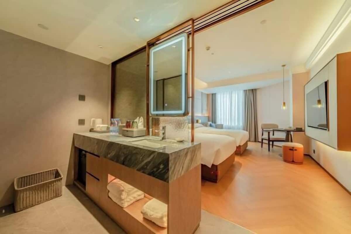 Una habitación de hotel moderna con un espejo grande, un tocador de mármol, una cama, un televisor y una zona de estar.