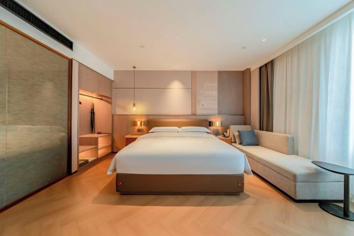 Ein modernes Hotelzimmer mit einem großen Bett, einer Couch, einem kleinen Tisch und Blick auf die Stadt.