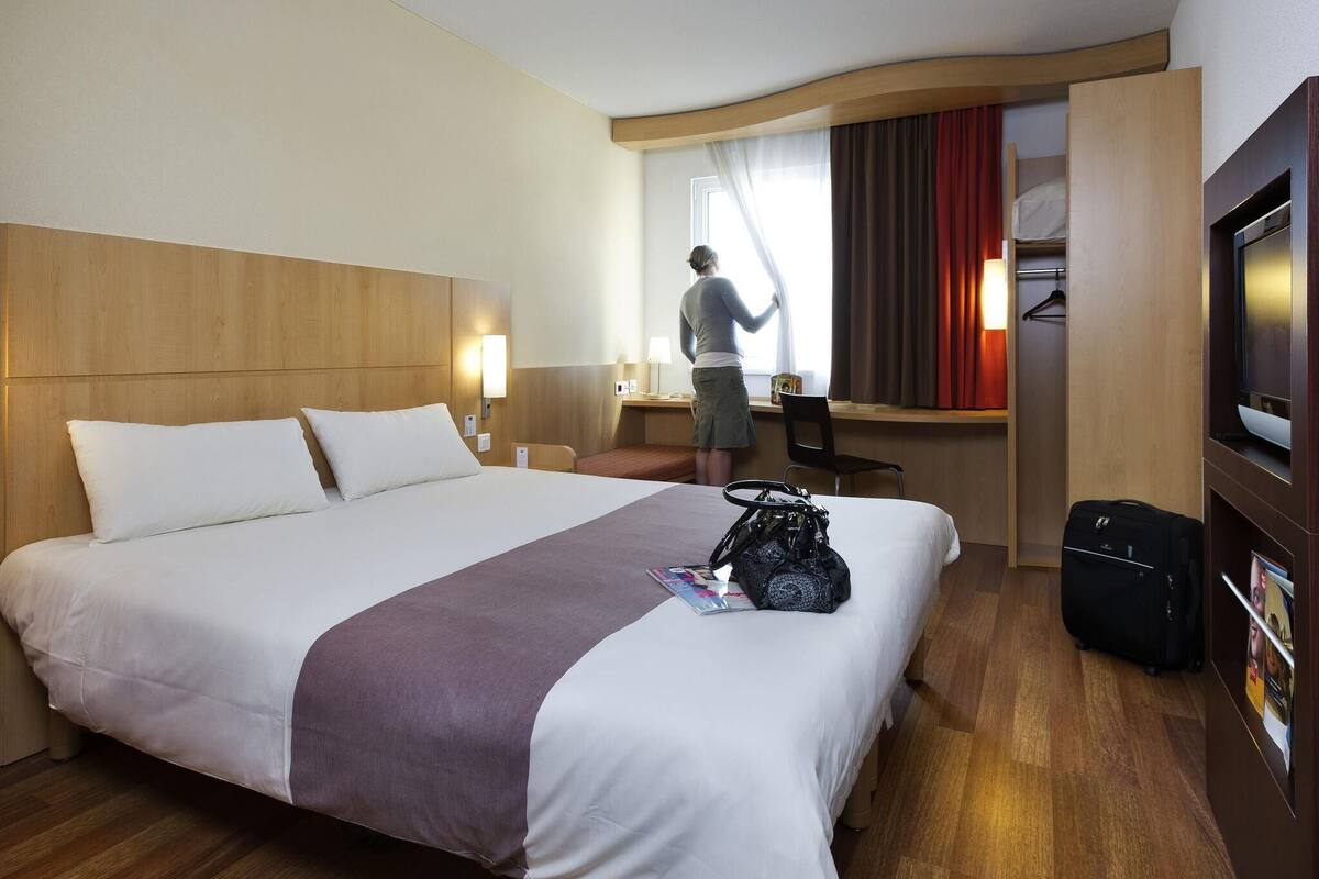 Una habitación de hotel con una cama grande, un escritorio, una silla, un televisor y una maleta.
