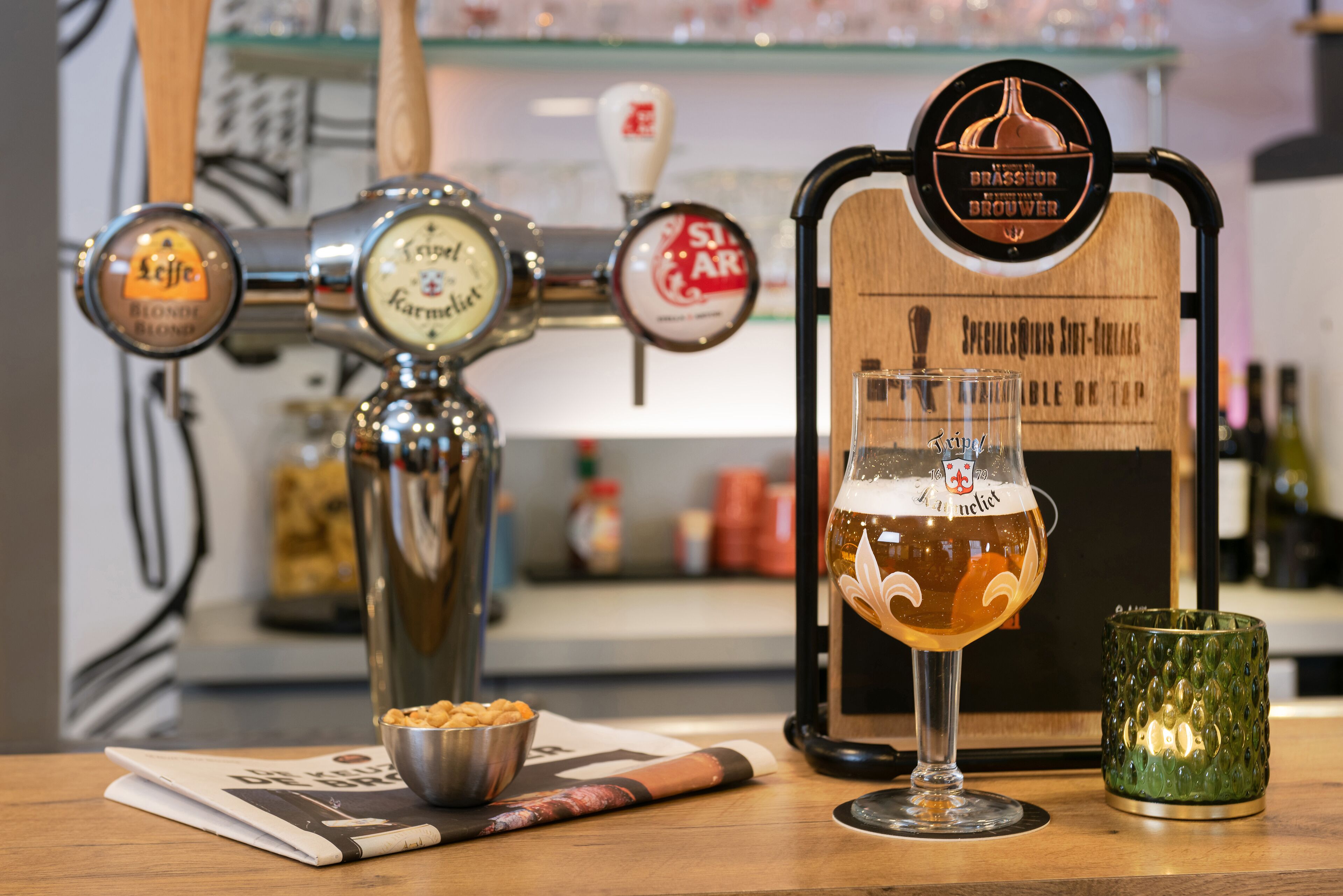 Una grifería con varias opciones de cerveza, una jarra de cerveza y una vela sobre una mesa.