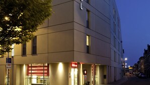 Un hotel moderno con un llamativo letrero de "Ibis", una entrada bien iluminada y una vista despejada de la calle.