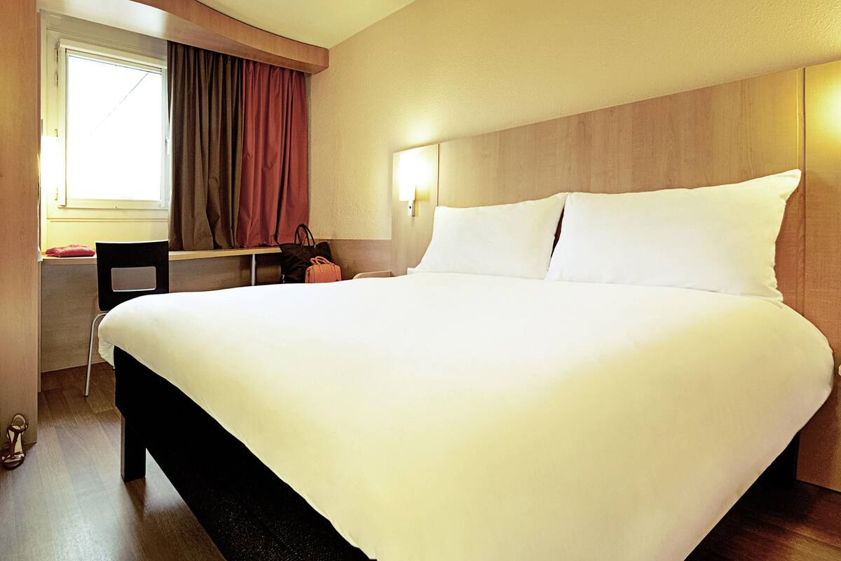 A hotel room with a large bed, a desk, and a chair.