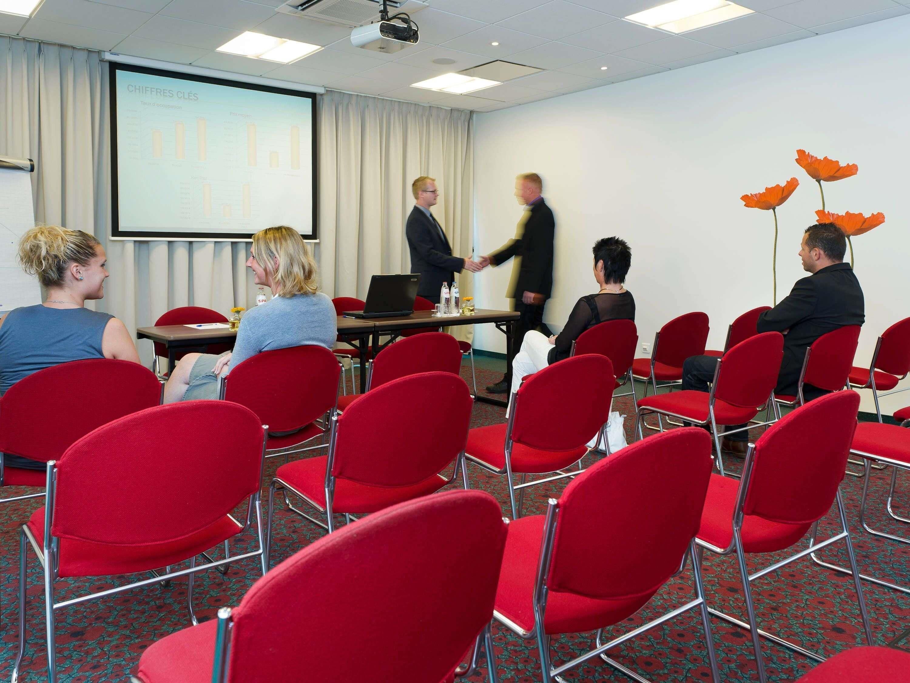 A conference room with red chairs, a projector screen, and a presentation.
