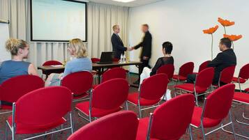 A conference room with red chairs, a projector screen, and a presentation.