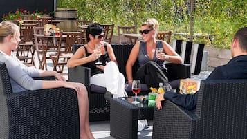 Een terras met rieten meubels, een tafel met drankjes, en een achtergrond van groen en een hek.