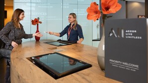 Un mostrador de recepción con pantalla digital, encimera de madera y un jarrón con flores.