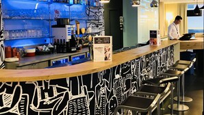 Zona de bar con diseño moderno, que incluye una barra con un tablero de menú, una variedad de botellas y un área de asientos con taburetes de bar.