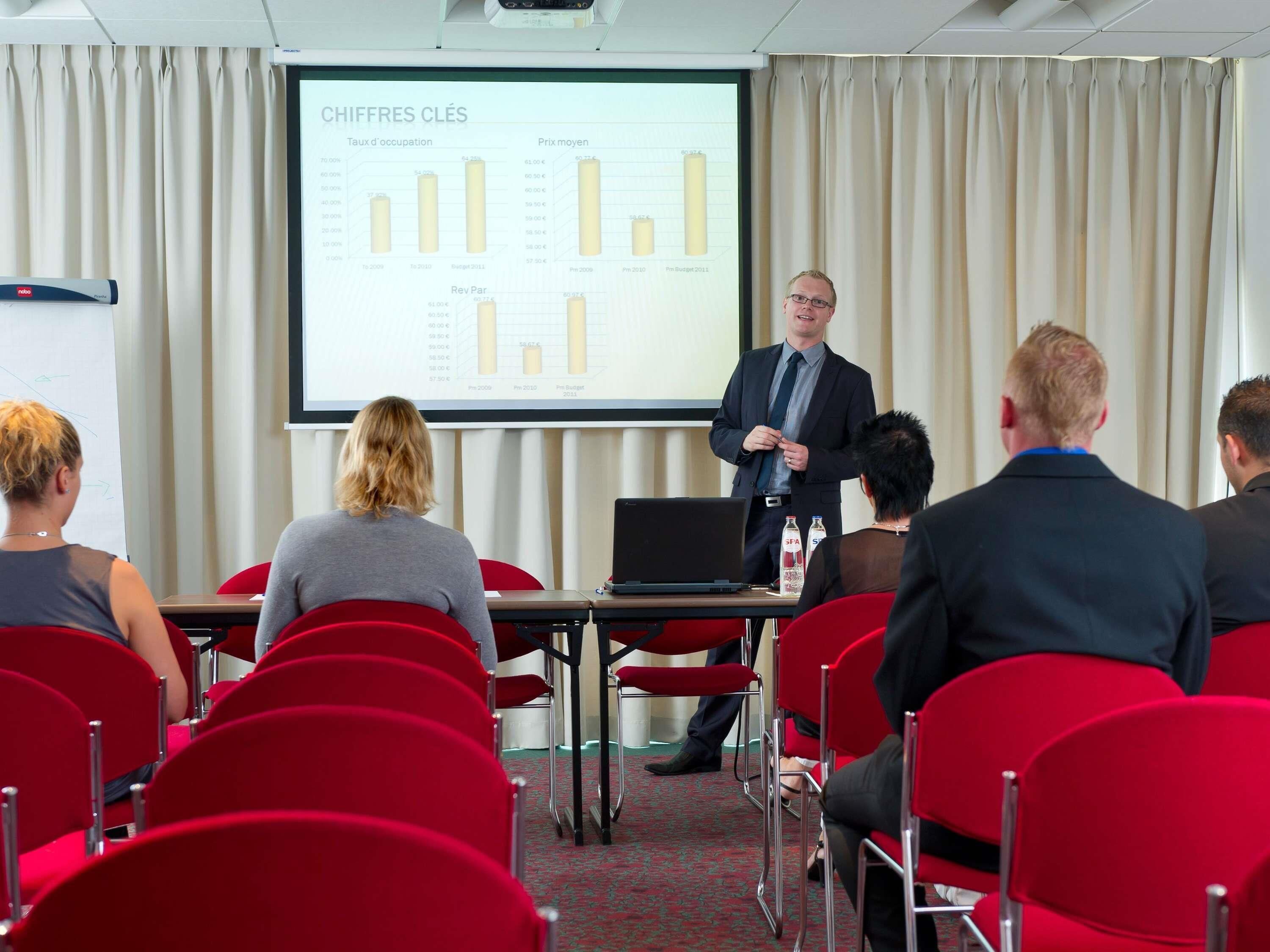 A conference room with a presentation screen displaying financial data, red chairs, and a projector.
