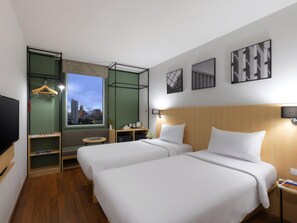 Een hotelkamer met twee bedden, een televisie, een raam met uitzicht over de stad en kunst aan de muur.