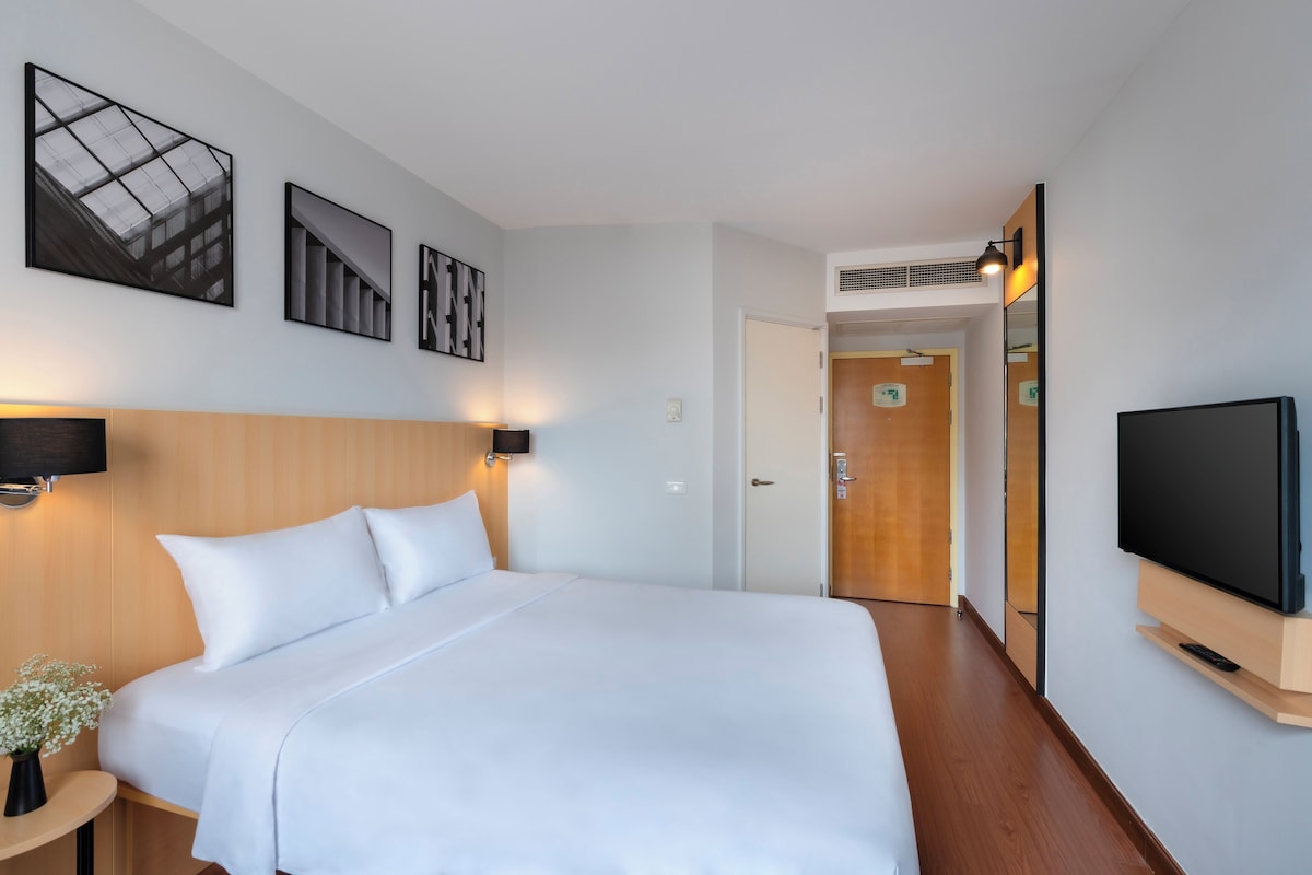 Een hotelkamer met een groot bed, een flatscreen televisie en kunstwerken aan de muur.
