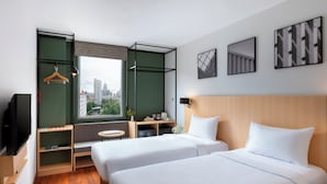 Een hotelkamer met twee bedden, een televisie, een bureau, een raam met uitzicht op de stad, en kunst aan de muur.