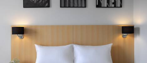 A hotel room with a wooden headboard, two wall-mounted lamps, a bed with white bedding, and three framed pictures on the wall.