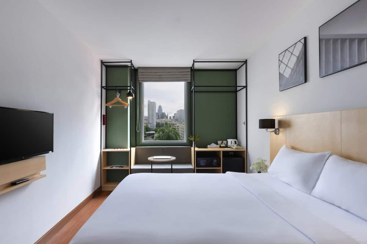 Une chambre d’hôtel moderne dotée d’un grand lit, d’une télévision, d’un bureau et offrant une vue sur la ville.