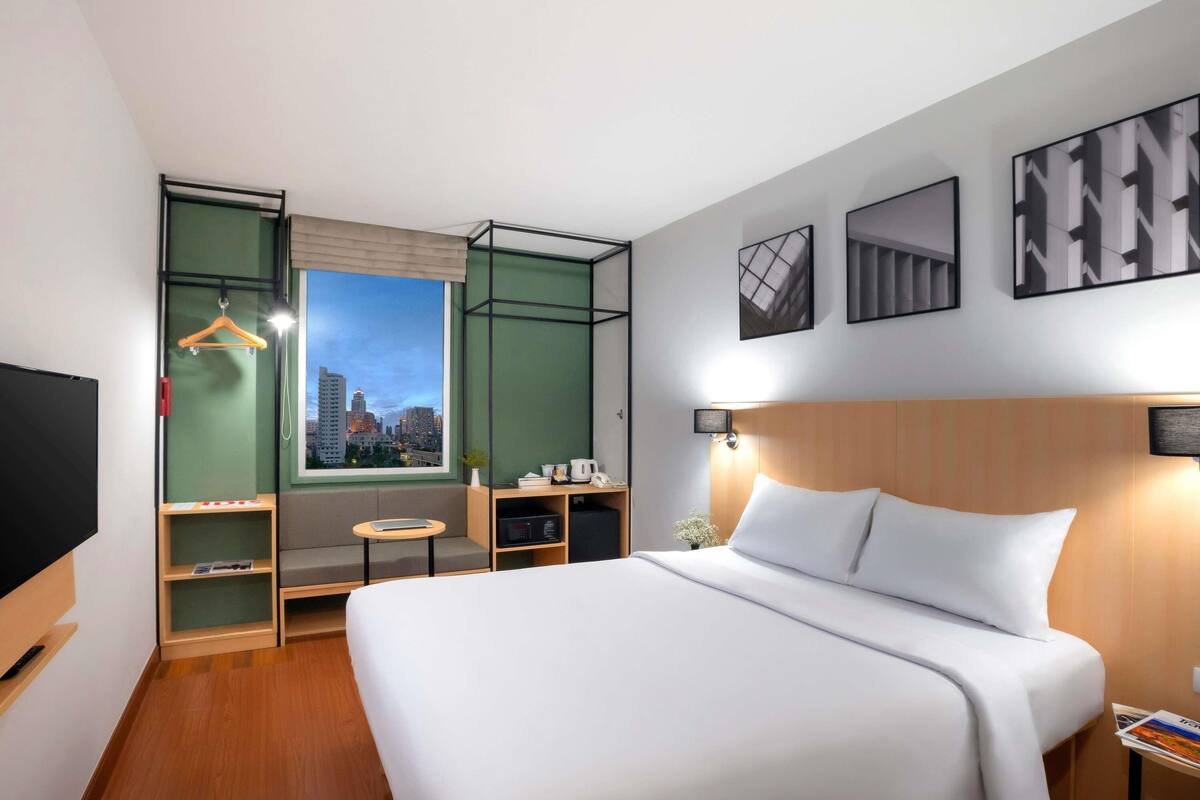 Een hotelkamer met een bed, een televisie, een raam met uitzicht op de stad, een bureau en een kledingkast.