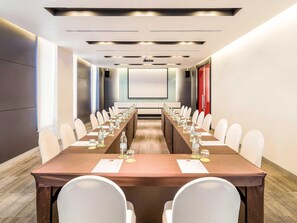 Une salle de conférence avec une longue table, des chaises blanches et un écran de projection.
