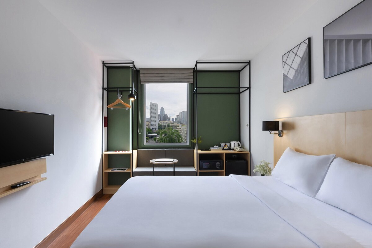 Habitación de hotel moderna con una cama grande, televisión, escritorio y vista a la ciudad.