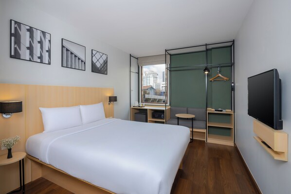 A modern hotel room with a large bed, a TV, a desk, and a view of the city.