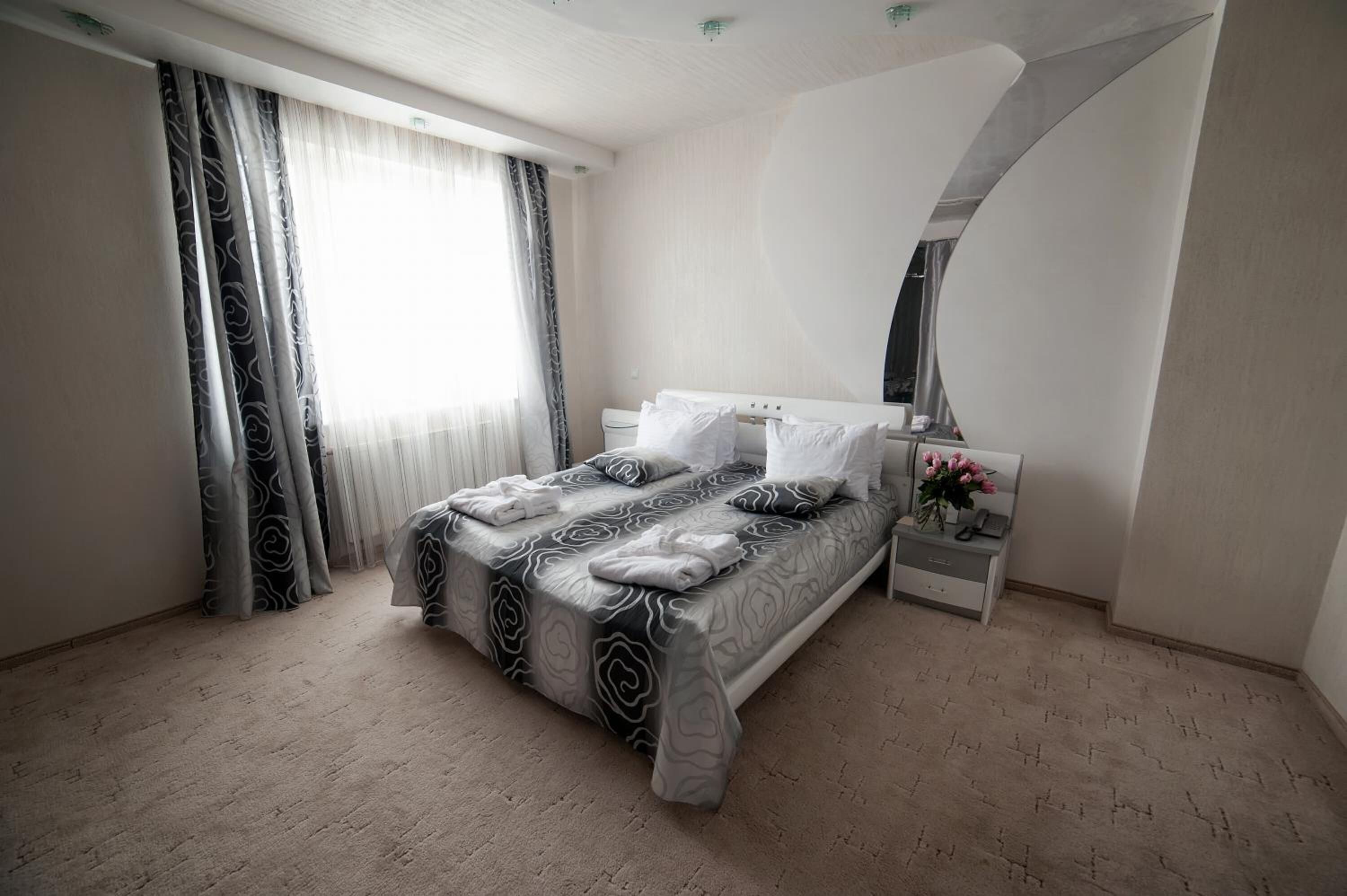 A bedroom with a bed, nightstand, and a large window with curtains.