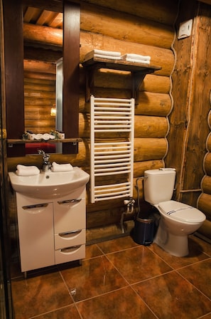 A bathroom with a wooden log wall, a white sink with two towels, a toilet, and a towel rack. - Praha Hotel (Uzhhorod)