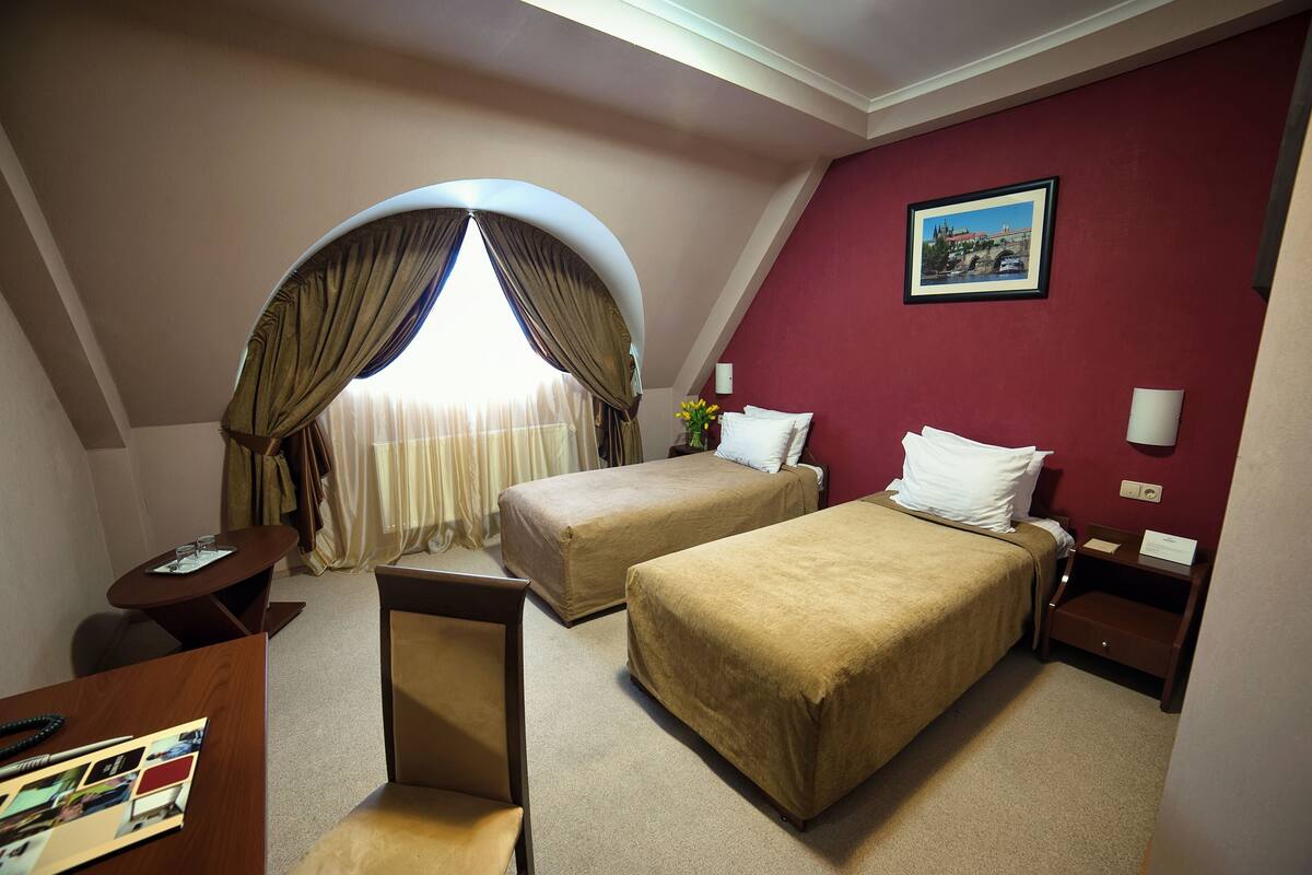 A hotel room with two beds, a desk, a chair, a small table, and a window with curtains.