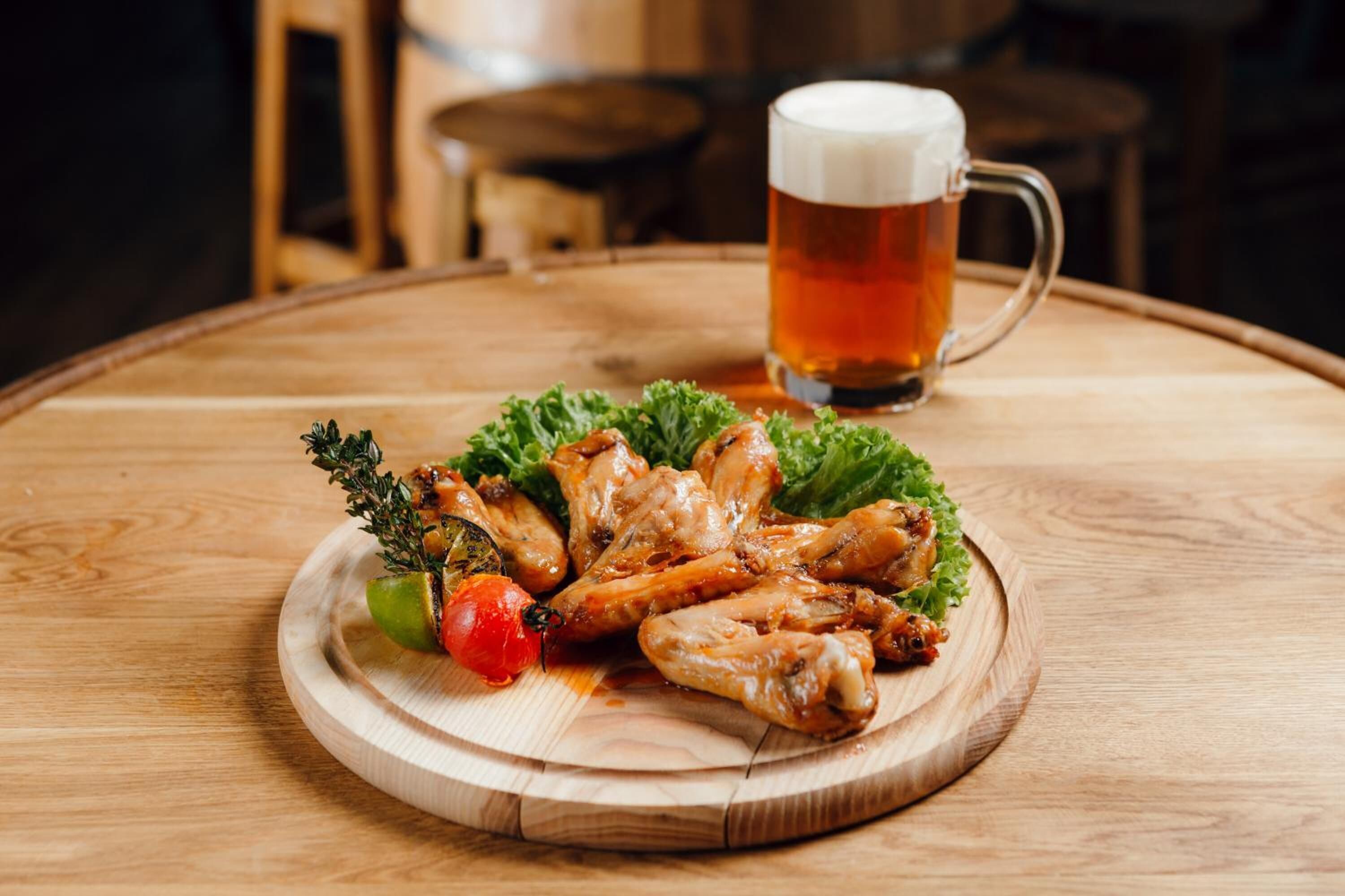 Ein Holztisch mit einem Teller gegrillten Hähnchenflügeln, einem Glas Bier und einem kleinen Salat auf einer Holzschneidebrett.