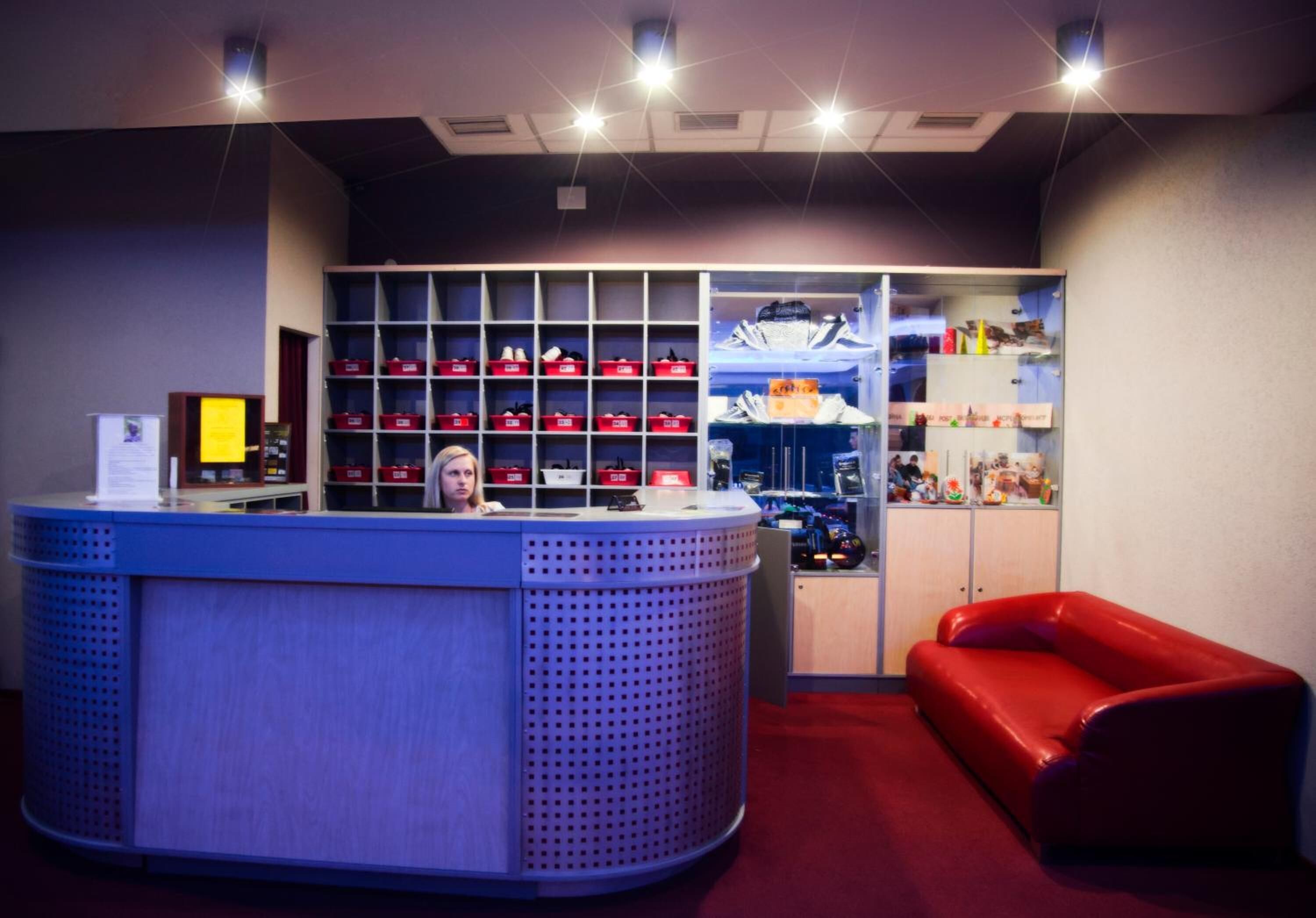 Un espace d’accueil comprenant un comptoir, des étagères avec des boîtes rouges, un canapé rouge et une vitrine contenant divers objets.
