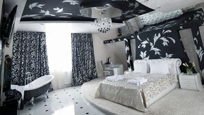Quarto de hotel moderno com uma cama grande, área de estar, banheira e mesa de vidro com bandeja.