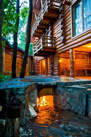 A log cabin with a stone fireplace, wooden deck, and a view of the surrounding forest. - Praha Hotel (Uzhhorod)