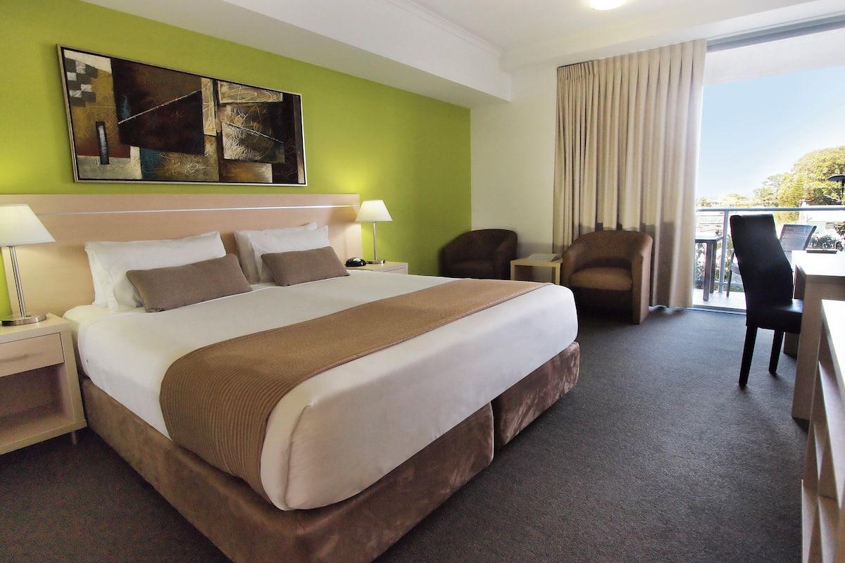 A hotel room with a large bed, two bedside tables, a chair, a desk, and a view of the outdoors.