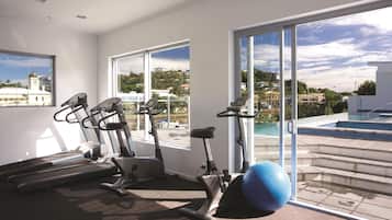 A gym with exercise equipment and a view of a swimming pool and buildings.