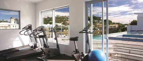 Un gimnasio con equipo de ejercicio y vistas a una piscina y edificios.
